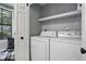 Functional laundry room with side-by-side washer and dryer units and storage shelves at 7708 Falcon Rest Cir, Raleigh, NC 27615