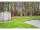 Backyard view with a storage shed, grassy area, concrete patio, and a wooded area in the background at 507 W Edwards St, Princeton, NC 27569