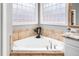 Close up of a corner bathtub with tiled surround, sleek faucets, and decorative statue, all within a modern bathroom at 7001 Millstone Ridge Ct, Raleigh, NC 27614
