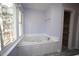 Bright bathroom featuring a large corner jacuzzi tub by the window and a doorway to a walk-in closet at 1501 Ramson Ct, Raleigh, NC 27603