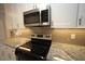 Close-up of stove and microwave featuring granite countertops and tiled backsplash at 1501 Ramson Ct, Raleigh, NC 27603