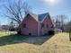 Rear and side view of a well-maintained brick home with a lush green yard and mature trees under a sunny sky at 1006 Stallings Rd, Durham, NC 27703