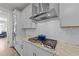 Close up of a cooktop with stainless steel hood, white cabinets, and neutral backsplash at 112 Ava Ct, Holly Springs, NC 27540