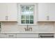 Close-up view of a white kitchen sink with marble backsplash and window between white cabinets at 1222 Dixie Trl, Raleigh, NC 27607