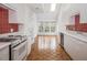 Well-lit kitchen with white cabinets, red tile backsplash, and wood flooring at 595 Weathersfield # A, Pittsboro, NC 27312