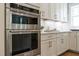 Close up of stainless KitchenAid double ovens, marble herringbone backsplash, and white cabinets with gold hardware at 109 W Markham Ave, Durham, NC 27701