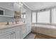Bright bathroom featuring double vanity sinks, decorative mirrors, and a tiled tub beneath a window at 3068 Benson Rd, Angier, NC 27501