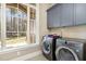 Laundry room with gray cabinets, stainless steel washer/dryer, and large window at 7936 Nc 42, Holly Springs, NC 27540