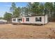 Single-story home with a cheerful red door and black shutters is nestled among tall pine trees at 92 Papoose Trl, Lillington, NC 27546