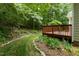 Lush backyard featuring a wooden deck, manicured lawn, mulch, and thriving plants at 4909 Willow Tree Ln, Clayton, NC 27520