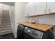 Modern laundry room with dark appliances, a wood countertop, and white cabinets for storage, and a door to the stairs at 209 Plyersmill Rd, Cary, NC 27519