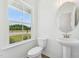 Powder room with pedestal sink, oval mirror, and toilet near a window with green landscape view at 269 Marvel Dr # 138, Rolesville, NC 27571