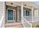 Inviting covered front porch with brick steps, stone pillars, railing, and a vibrant green door at 1106 Bellenden Dr, Durham, NC 27713