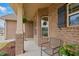Close up of a well-maintained front porch with brick accents, hanging plants, and a cozy chair at 38 Parkside Dr, Lillington, NC 27546