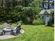 Charming backyard featuring a stone fire pit, Adirondack chairs, and shed surrounded by lush greenery at 3708 Wesley Ridge Dr, Apex, NC 27539