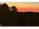 A gorgeous fiery sunset creates a dramatic backdrop over the backyard trees from this perspective at 112 Sire Ct, Holly Springs, NC 27540