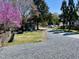 Backyard with gravel driveway, wooden playset, blooming tree, and garden beds, under a bright blue sky at 1426 N Roxboro St, Durham, NC 27701