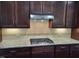 Close-up on the kitchen's granite countertop, gas cooktop, tile backsplash, and dark cabinets at 621 Rockcastle Dr, Cary, NC 27519