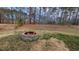 Backyard featuring a stone fire pit, set within a grassy lawn and a backdrop of trees, ideal for outdoor gatherings at 104 Vinewood Pl, Holly Springs, NC 27540