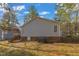 View of the home's gray siding, brick foundation, and wooden deck with stairs in a wooded lot at 1107 Goldendale Dr, Durham, NC 27703