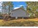 View of the home's gray siding, brick foundation, and wooden deck with stairs in a wooded lot at 1107 Goldendale Dr, Durham, NC 27703