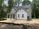 New two-story home with gray siding, black roof, and a covered front porch surrounded by wooded landscape at 5036 Trotter Dr, Raleigh, NC 27603