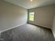 Bright bedroom with neutral walls, plush gray carpeting, and natural light from a window overlooking a green space at 712 Swim Cave Ln, Wendell, NC 27591
