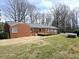 Rear exterior showcasing a two-car garage, brick exterior, wooden deck and ramp with beautiful, mature trees surrounding it at 3015 Nc Hwy 87 South, Graham, NC 27253