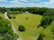 Aerial view of a sprawling green field with a tree, a fence, and a barn in the distance at 4811 New Sharon Church Rd, Hillsborough, NC 27278