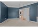 Inviting bedroom with neutral carpet, blue accent wall, and white trim and open door to another room at 1046 Upchurch Farm Ln, Cary, NC 27519