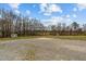 Large gravel parking pad with shed in the distance, surrounded by mature trees and a grassy yard at 4194 Abattoir Rd, Angier, NC 27501