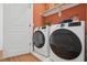 Functional laundry room with white front-load washer and dryer, wooden shelf and an orange accent wall at 1028 Zelkova Ln, Chapel Hill, NC 27517
