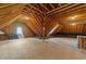 Unfinished attic featuring exposed wooden beams, plywood flooring, and natural light from a small window at 10540 Byrum Woods Dr, Raleigh, NC 27613
