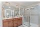 Bathroom featuring dual sinks, wood cabinetry, and glass-enclosed shower with tiled walls at 2418 Pecan Ridge Way, Apex, NC 27502