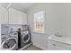 Well-lit laundry room featuring white cabinets, a sink, and modern washer and dryer units at 6116 Wilkinsburg Rd, Raleigh, NC 27612