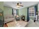 Bright Bedroom with a crib, gray chair, ceiling fan, area rug, and two windows with blue curtains at 215 Seventh St, Wake Forest, NC 27587