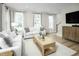 Bright living room with large windows, plush white couches, modern decor, wooden table and access to stairs at 603 Silverado Sunset Loop, Wendell, NC 27591