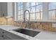 A modern kitchen sink features a gooseneck faucet, stone countertops, and a mosaic tile backsplash underneath a large window at 7100 Hasentree Club Dr, Wake Forest, NC 27587