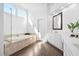 Bright bathroom featuring a soaking tub with tiled surround, vanity with marble countertop, and hardwood flooring at 101 Listokin Ct, Cary, NC 27519