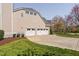 Three-car garage with white doors and driveway surrounded by manicured landscaping and greenery at 101 Listokin Ct, Cary, NC 27519