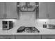 Close up of gas cooktop, stainless steel vent hood, gray cabinetry and quartz countertops in the kitchen at 505 Marion Hills Way, Knightdale, NC 27545