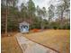 Backyard shed on stone paver pathway amidst fenced in wooded lot with mature trees and grass at 45 Carriden Dr, Youngsville, NC 27596
