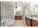 Bathroom with wood cabinetry, tile floor, two sinks, soaking tub, and modern lighting at 162 Arabella Ct, Cary, NC 27518