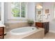 Bright soaking tub with tiled surround, large window, and white shutters at 2739 Elderberry Ln, Apex, NC 27539