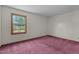A plain bedroom with purple carpet shows a window with a view of trees and a fenced yard at 5437 Grasshopper Rd, Raleigh, NC 27610