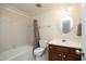 Bright bathroom with a tiled tub/shower combo, wood vanity and round mirror at 8310 Wycombe Ln, Raleigh, NC 27615