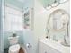 Bathroom featuring a toilet, shelf, rounded mirror and vanity sink, complemented by soft blue walls at 10836 Connally Ln, Raleigh, NC 27614