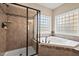 Bathroom featuring a glass door shower and a white soaker tub with tiled surround and privacy windows at 9 Water Stone Ct, Durham, NC 27705