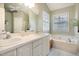 Bright bathroom featuring double sinks, a soaking tub under a large window, and contemporary white cabinetry at 12 Montcrest Dr, Durham, NC 27713