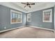 Neutral carpeted bedroom featuring a ceiling fan, tray ceiling, and natural light through large windows at 220 Shawnee Dr, Louisburg, NC 27549